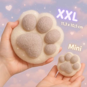 Puede incluir: Dos almohadillas de fieltro con forma de pata de gato, una grande y otra pequeña, en crema y marrón. La almohadilla más grande está etiquetada como "XXL" y mide 11,3 x 10,5 cm. La almohadilla más pequeña está etiquetada como "Mini". El fondo es rosa y morado.