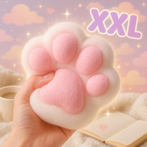 Puede incluir: Un cojín blanco con forma de pata de gato con almohadillas rosas. El texto "XXL" es de color púrpura. El fondo presenta una estética suave y soñadora con nubes y destellos. Se ven una taza y un libro.