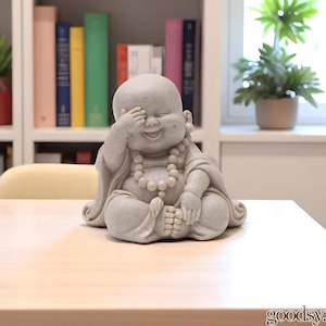K&ouml;nnte beinhalten: Hellgraue, l&auml;chelnde Buddha-Statue mit einer Hand, die die Augen bedeckt. Die Statue tr&auml;gt eine Perlenkette und ein drapiertes Gewand. Der Buddha sitzt auf einer hellen Holzoberfl&auml;che.