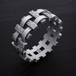 May include: A silver ring with a unique design featuring a woven pattern with floral details. The ring is marked with the number "925" on the side.