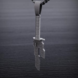 Könnte beinhalten: Eine silberfarbene Halskette mit einem Anhänger in Form eines stilisierten Schwertes. Der Anhänger hängt an einer dunklen Kette und hat eine strukturierte Oberfläche. Das Schwertdesign umfasst einen gewickelten Griff und eine detaillierte Klinge.