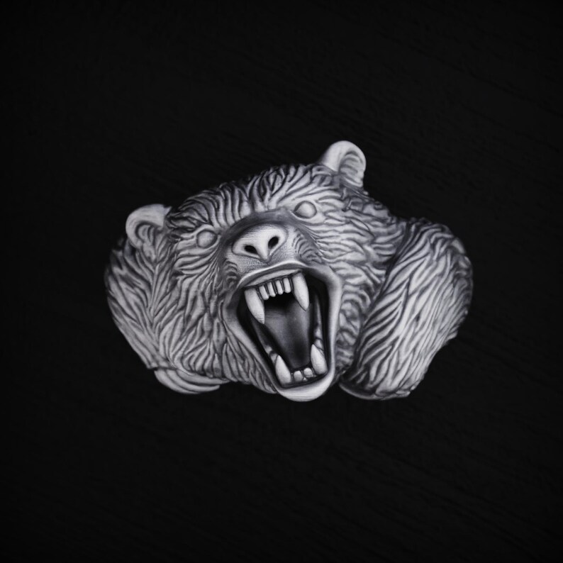 May include: A detailed silver sculpture of a bear's head with its mouth open, showing sharp teeth. The bear's fur is textured and realistic.