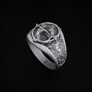 May include: A silver ring with a detailed design of two figures fighting with swords. The ring is engraved with the number "925" on the side.