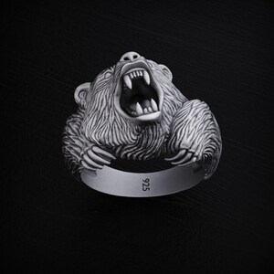 May include: A silver ring with a detailed, roaring bear head design. The ring is marked with "925" on the band.