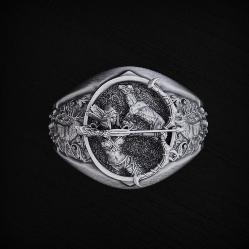 May include: A silver ring with a detailed design of a woman holding a bow and arrow, with a deer and other wildlife surrounding her.