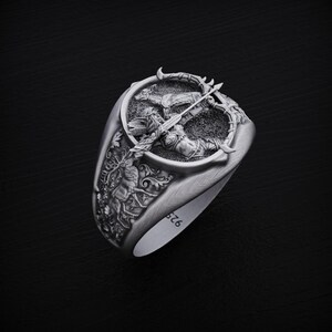 May include: A silver ring with a detailed design of a figure holding a bow and arrow. The ring is engraved with the number "576".