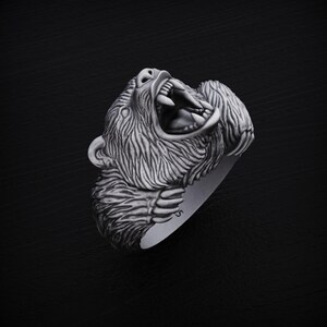 May include: A silver ring featuring a detailed, roaring bear head design. The bear's mouth is open, showing sharp teeth, and its fur is intricately sculpted.