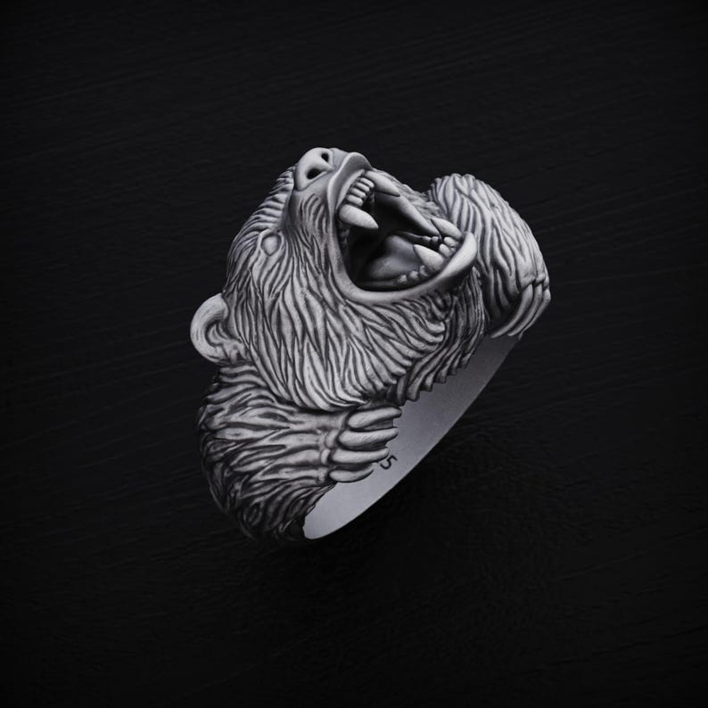 May include: A silver ring featuring a detailed, roaring bear head design. The bear's mouth is open, showing sharp teeth, and its fur is intricately sculpted.