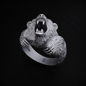May include: A silver ring featuring a detailed, roaring bear head. The ring is marked with "925" on the band.