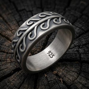 May include: A wide silver ring featuring a raised, continuous vine-like pattern with curved, scroll-shaped leaves against a darkened, oxidized background. The interior of the band is smooth and clearly stamped with the hallmark 925 for sterling silver.