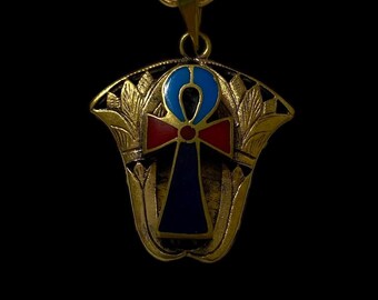 Op de afbeelding: Goudkleurige hangerketting met een Ankh-symbool met blauwe, rode en gouden accenten. De hanger hangt aan een fijne ketting. De ketting heeft een Egyptisch thema.