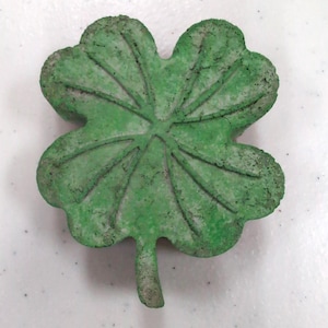 Puede incluir: Un adoquín de jardín de concreto verde en forma de trébol de cuatro hojas.