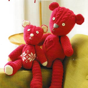 Op de afbeelding: Twee rode gebreide teddyberen. De grotere beer is ongeveer 50 cm lang en de kleinere beer is ongeveer 35 cm lang. De beren hebben witte accenten op hun oren, poten en een sneeuwvlokontwerp op de kleinere beer. Het woord "Hayfield" is in rode letters geschreven.