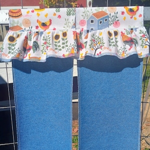 May include: Blue denim kitchen curtains with a decorative top featuring a white ruffle. The ruffle is patterned with sunflowers, chickens, and a small blue house. The top panel has a white background with a repeating pattern of chickens, apples, and a barn.