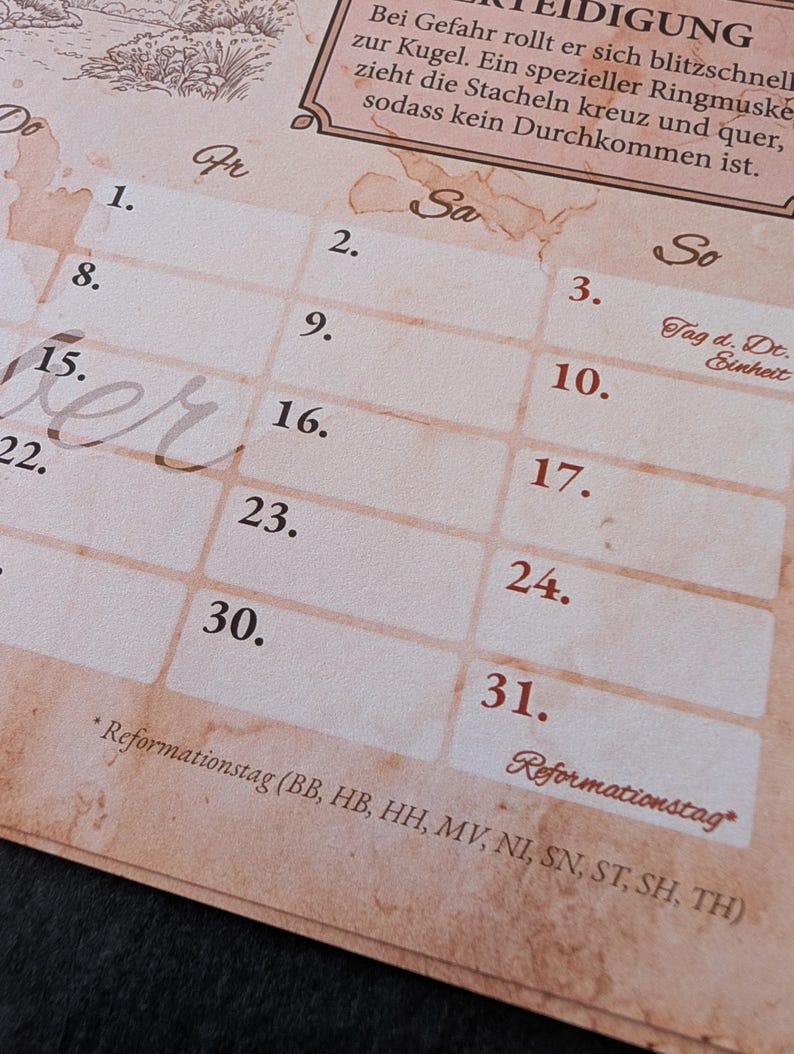 Op de afbeelding: Een beige kalenderpagina met een vintage perkamenttextuur met een raster van genummerde dagen. De tekst bevat Duitse koppen zoals Fr, Sa en So, samen met een kader met Duitse tekst over verdediging en de feestdag Reformationstag.