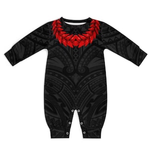 May include: Black baby romper with a tribal pattern and a red floral design around the neckline. The long-sleeved romper has snaps at the bottom for easy changes. The overall design is a mix of traditional and modern elements.