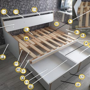 May include: A white bed frame with a headboard and two large drawers. The bed frame has a wooden slat support system. The drawers have silver handles. The bed frame is against a textured gray wall.