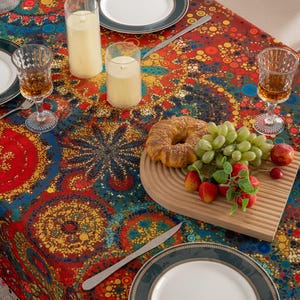 May include: A colorful tablecloth with a vibrant pattern of red, blue, and yellow circles. The table is set with plates, glasses, silverware, candles, and a wooden cutting board with fruit and pastries.