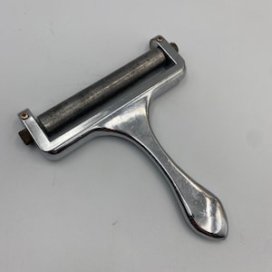 May include: A shiny, chrome-plated cheese slicer with a roller blade and a handle. The cheese slicer is designed for easy and efficient slicing of cheese. The handle is ergonomically designed for a comfortable grip.