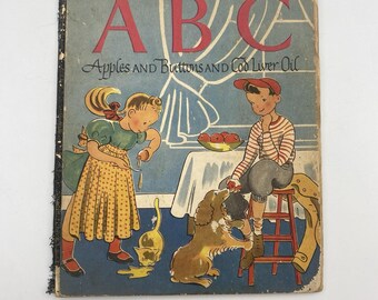 May include: Vintage ABC book cover with the title in large red letters. The cover features illustrations of children, a dog, and a cat. The text below the title reads "Apples and Buttons and Cod Liver Oil."