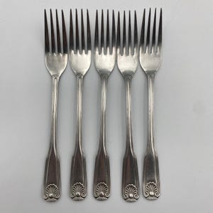 May include: A set of five silver-toned metal forks arranged vertically. Each fork features four tines, a slender handle with a vertical ridge, and a decorative shell-shaped motif embossed at the base of the handle. The finish is smooth and metallic.