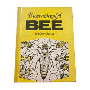 May include: A vintage book titled "Biography of A BEE" by Harry Smith. The cover is yellow with black text and illustrations of bees and a honeycomb pattern. The book has a worn appearance.