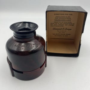 May include: A vintage red-brown Chromat-O-Scope viewer with a black top and a matching box. The viewer has the text "MADE BY FROM LOS ANGELES" and the box has instructions for use. The viewer is designed to enlarge slides.