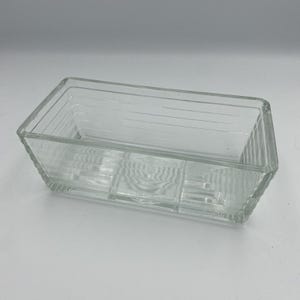 May include: A clear, rectangular glass dish with a ribbed design. The dish has a rectangular shape and is likely used for serving or storage. The glass is transparent, allowing the contents to be visible.