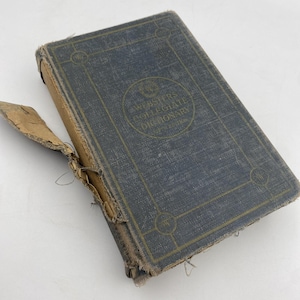 May include: An antique Webster's Collegiate Dictionary, 5th Edition, with a blue cover and gold lettering. The book shows signs of wear, with a torn spine and frayed edges, suggesting its age and use. The title is prominently displayed.