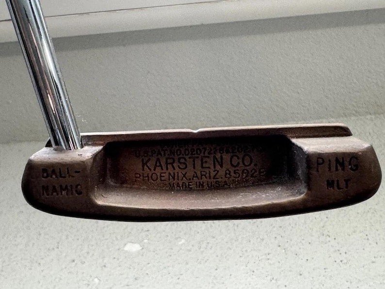May include: Vintage Ping MLT golf putter with a brown head and a silver shaft. The putter head has the text "KARSTEN CO. PHOENIX, ARIZ. 85028 MADE IN U.S.A." and "BALL-NAMIC" and "PING MLT" on the head.