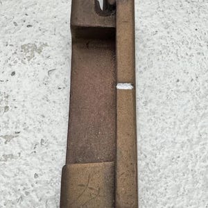 May include: A bronze-colored golf putter with a silver shaft. The putter head has a rectangular shape with a small white line. The putter has a worn, textured appearance.