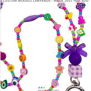 May include: A beaded lanyard featuring colorful plastic beads in various shapes including fruits, animals, flowers, and smiley faces. The text REAL CUSTOMER DESIGNS CUSTOM BEADED LANYARDS MADE JUST FOR YOU is visible at the top. A purple bow and metal clasp are attached.