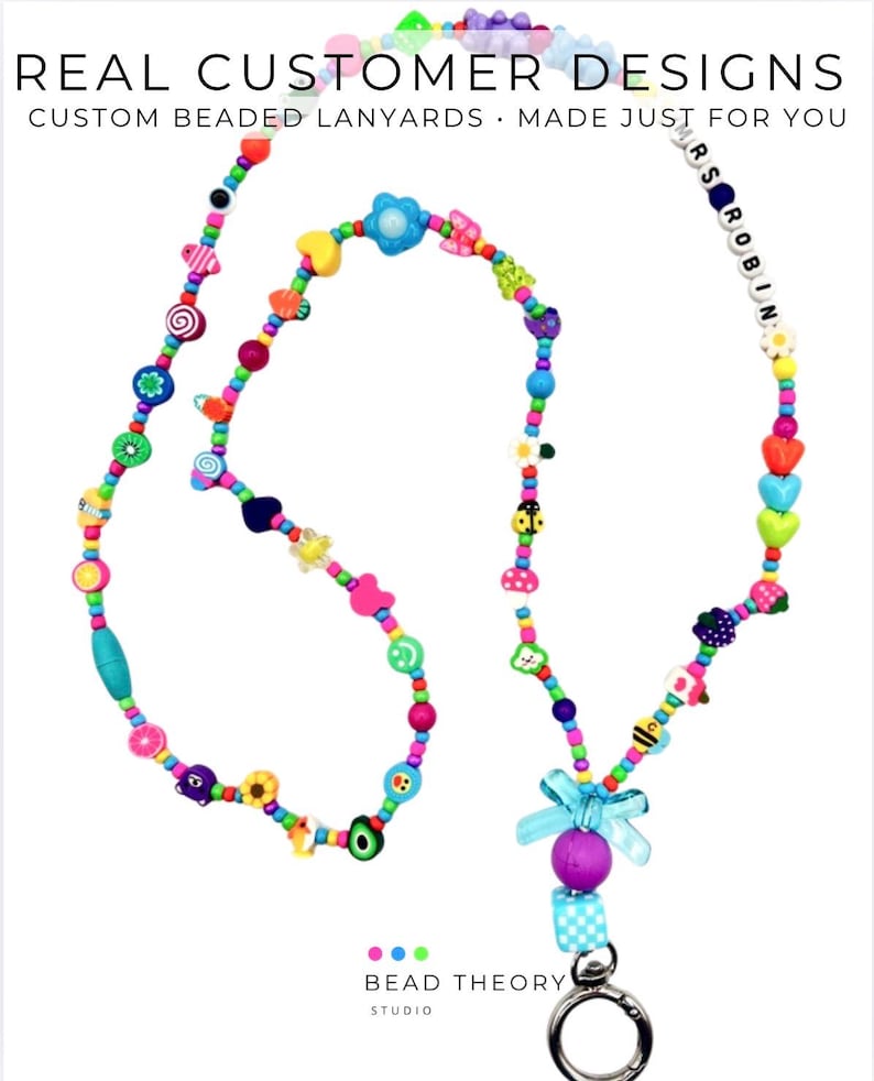 May include: A colorful beaded lanyard featuring a variety of shapes including hearts, flowers, fruits, and a ladybug. The beads are strung on a cord and include a section with the text MRS ROBIN. A light blue bow and a metal clasp are at the bottom.