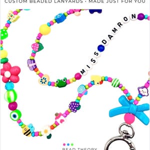 May include: A colorful beaded lanyard featuring a variety of shaped beads including flowers, frogs, butterflies, and a blue bow. The lanyard includes white letter beads spelling MISS DAMRON and a silver metal lobster clasp at the bottom end.