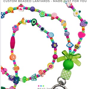 May include: A custom beaded lanyard featuring a variety of colorful charms including fruits, animals, flowers, and geometric shapes. The lanyard includes a green translucent bow, a large green bead, a checkered cube, and a silver metal lobster clasp.