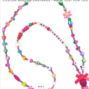 May include: A colorful beaded lanyard featuring a variety of shaped beads including flowers, fruits, and geometric patterns. The text "MRS STRUBLE" is spelled out in white letter beads. A bright pink bow and a metal clasp are attached at the end.