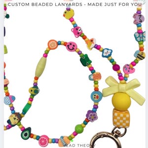 May include: A colorful beaded lanyard featuring various shaped charms including fruits, animals, and smiley faces. The lanyard includes a yellow bow, a yellow sphere, and a yellow and white checkered cube attached to a gold-toned metal lobster clasp.