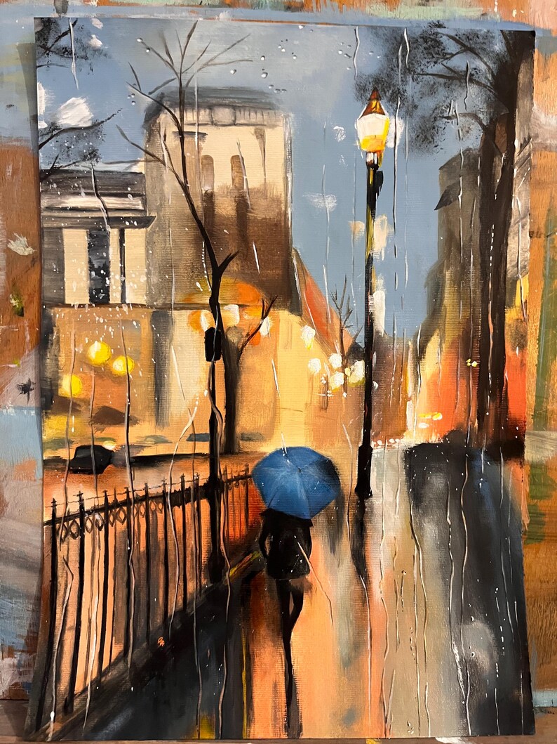 May include: An oil painting shows a rainy city street at night. A person with a blue umbrella walks along a wet pavement. Streetlights illuminate the buildings and the rain. The color palette includes blues, oranges, and browns.