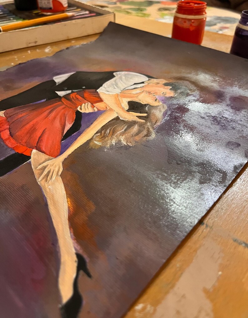 May include: An original painting depicts a couple dancing. The woman wears a red dress, and the man is in a black suit with a white shirt. The artwork is on a dark background with visible brushstrokes and paint splatters, suggesting an artistic process.