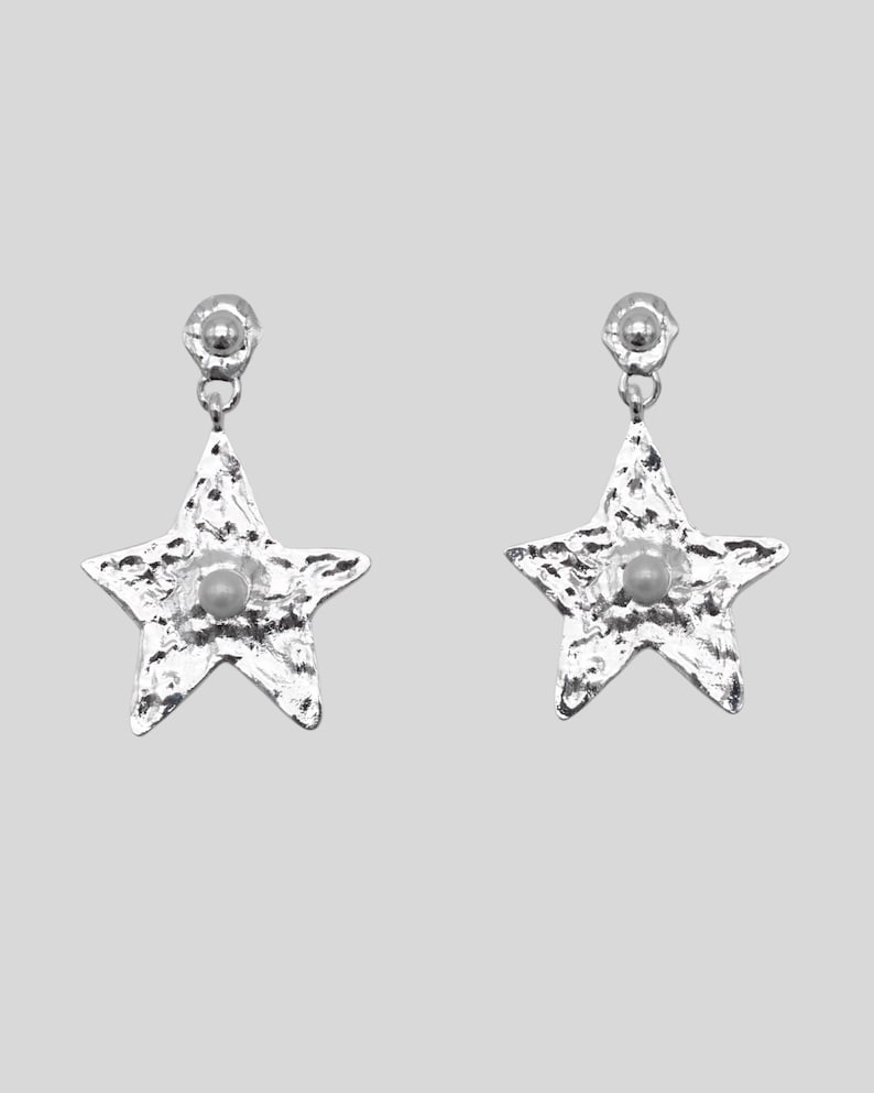 Pu&ograve; includere: Un paio di orecchini a forma di stella color argento. Ogni orecchino presenta una superficie strutturata e una piccola perla rotonda al centro. Gli orecchini hanno un perno e una piccola sfera sulla parte superiore per l'attacco.