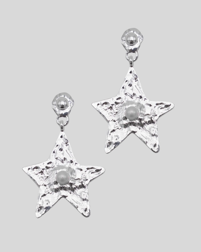 Pu&ograve; includere: Un paio di orecchini a forma di stella color argento. Ogni orecchino ha una superficie strutturata e una piccola perla rotonda al centro. Gli orecchini pendono da un piccolo perno rotondo.