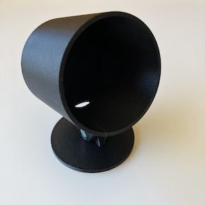 Könnte beinhalten: Eine mattschwarze Instrumentenhalterung bestehend aus einem zylindrischen Gehäuse auf einem runden Sockel. Das Bauteil verfügt über ein verstellbares Drehgelenk, das den Becher mit dem Standfuß verbindet, sowie eine kleine Öffnung am Boden.