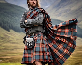 May include: A person wearing a traditional Scottish kilt outfit. The kilt features a plaid pattern in teal, orange, and navy blue. The outfit includes a gray jacket, belt, sporran, and a matching plaid shawl. The background shows a mountain range.