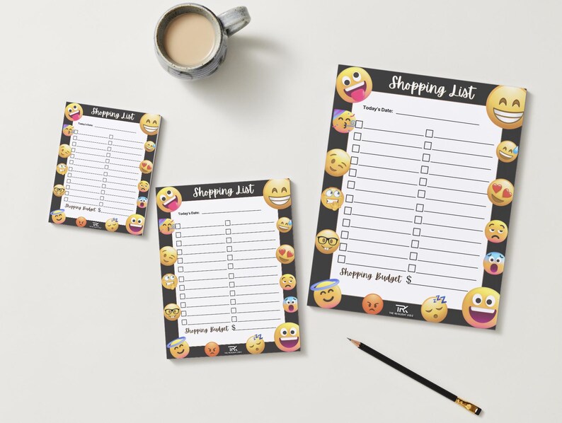 May include: Three shopping list notepads with a black border and emoji designs. The notepads have a white interior with lines and check boxes. The text "Shopping List" is at the top of each notepad. A pencil and a mug of coffee are also in the image.