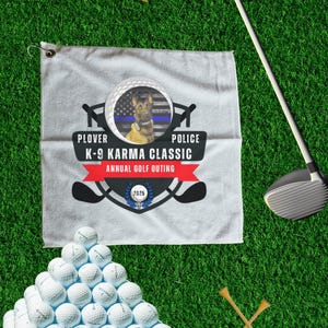 Puede incluir: Una toalla de golf blanca con un logotipo negro y azul que dice "Plover Police K-9 Karma Classic Annual Golf Outing 2023". El logotipo presenta un perro pastor alemán con una placa de policía.