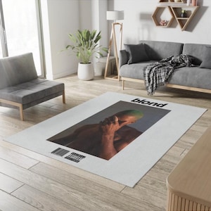 Puede incluir: Una alfombra blanca con una imagen en blanco y negro de un hombre con el pelo verde. La alfombra tiene la palabra "blond" impresa en letras negras.