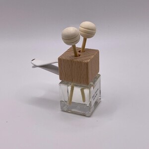 May include: A clear glass air freshener with a wooden top and two wooden ball diffusers. The air freshener has a white clip for attaching to a car vent. The text "Tidy Home Service" is visible on the glass.