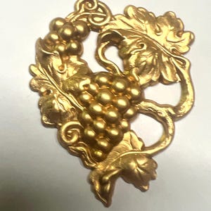 May include: A gold-colored decorative grape cluster with leaves and vines. The detailed design features a bunch of grapes, leaves, and curling vines, all in a metallic gold finish. This ornate piece is likely a decorative element.
