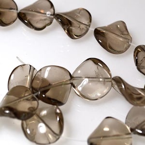 May include: A strand of translucent, smoky quartz beads. The beads are teardrop-shaped, with a faceted surface, and are strung on a thin, clear cord. The beads are a light brown color and are arranged against a white background.