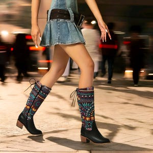 May include: Black knee-high boots with a colorful geometric pattern. The boots have a block heel and a lace-up detail at the back.